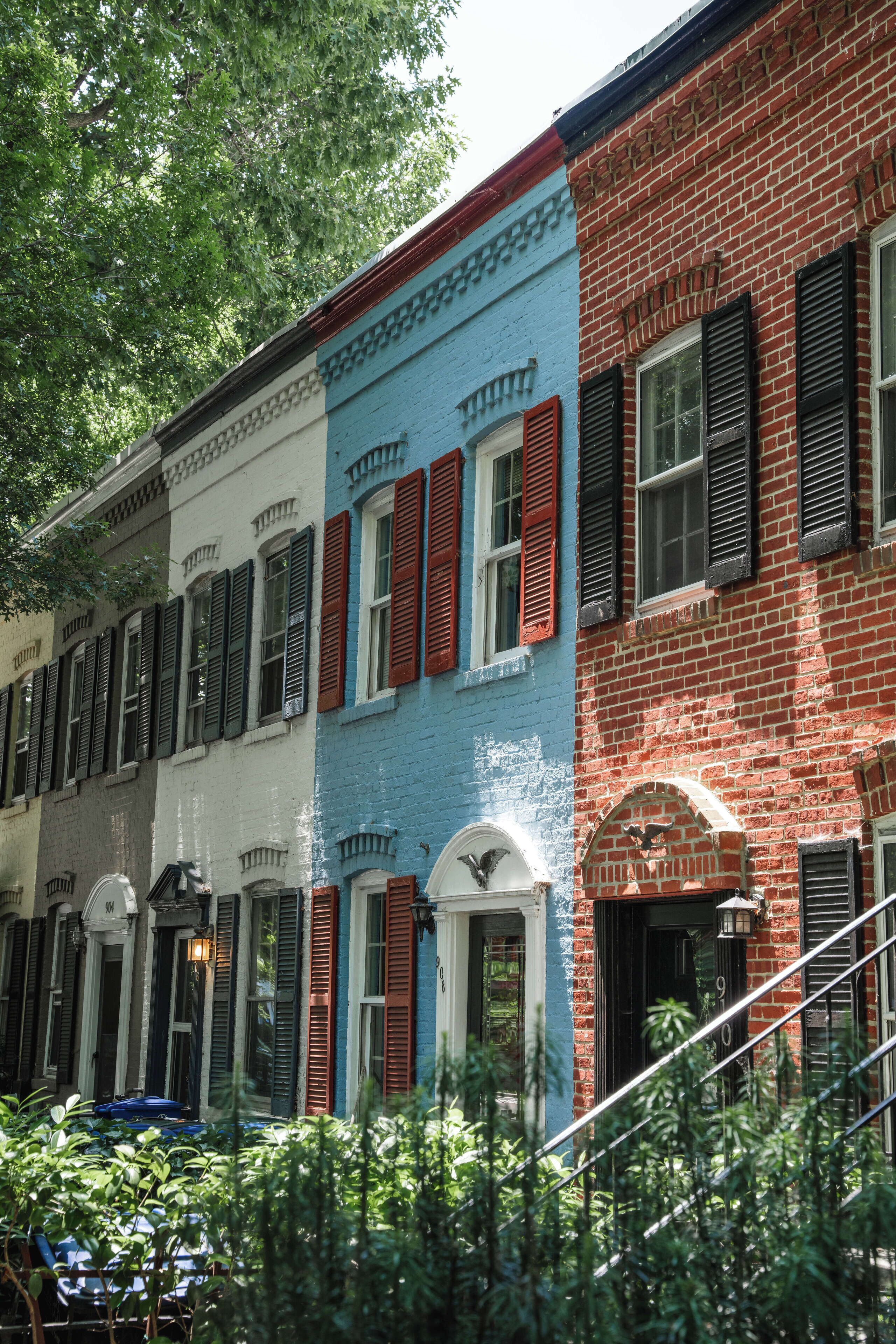 Una hilera de casas de pueblo coloridas con fachadas rojas, blancas y azules, contraventanas negras y un farol.