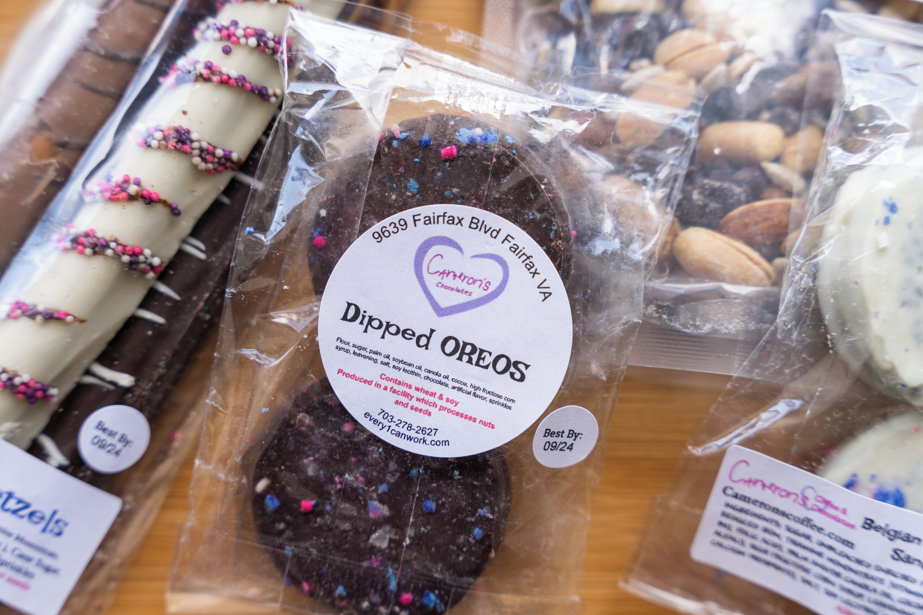 A variety of packaged chocolates, including dipped oreos and other confections, displayed on a wooden surface.
