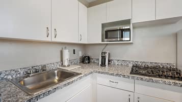 A kitchen with white cabinets, a stainless steel sink, a microwave, a coffee maker, and a gas stove.