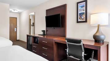 A hotel room with a bed, a desk with a chair, a television, a lamp, and a framed picture on the wall.