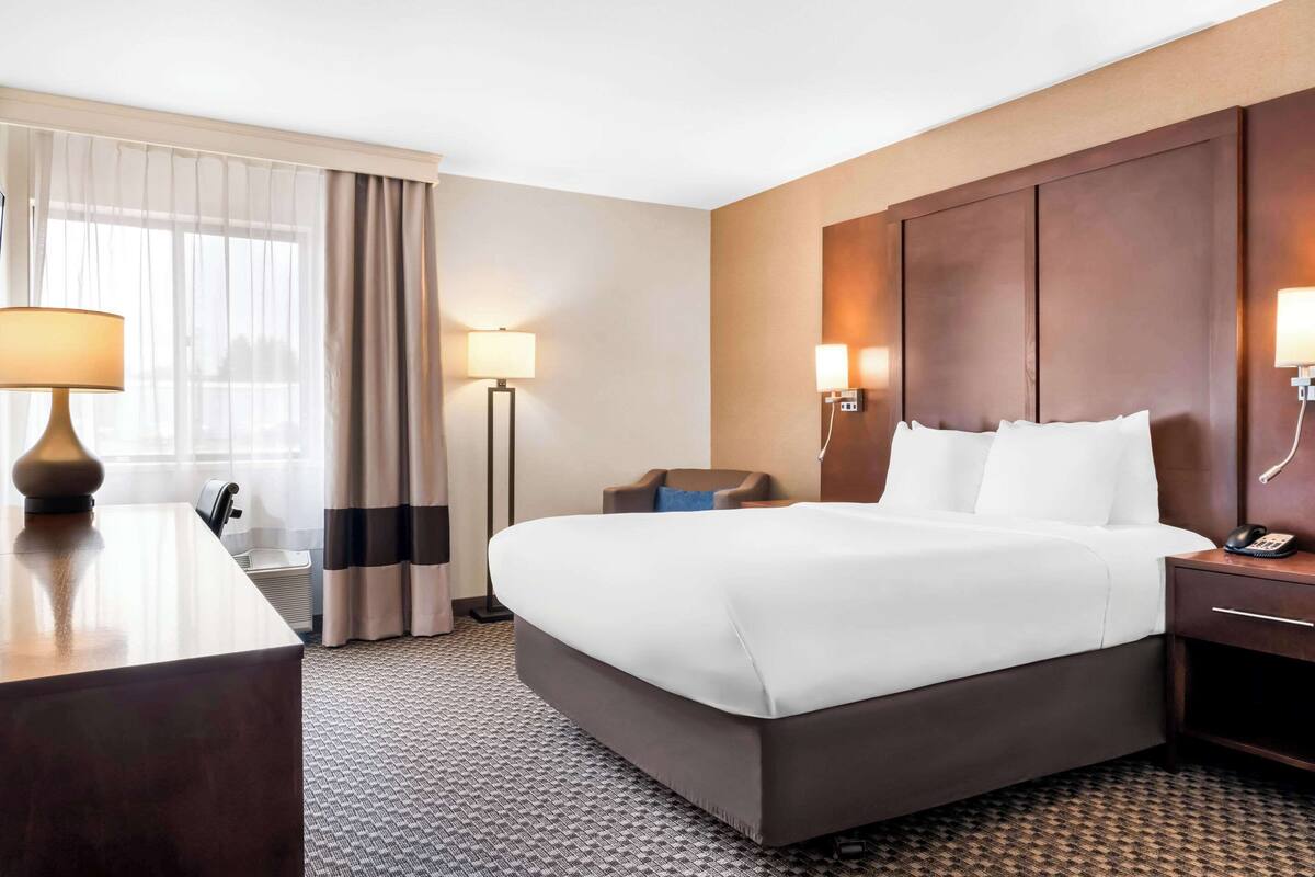 Een hotelkamer met een groot bed, nachtlampjes, een bureau en een stoel.