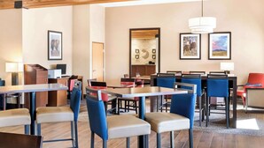 Un espace de restauration d’hôtel comprenant plusieurs tables et chaises, des poutres en bois au plafond et des œuvres d’art encadrées accrochées aux murs.