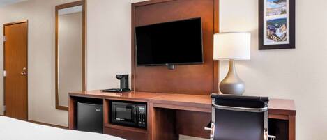 A hotel room with a bed, a desk with a flat-screen TV, a coffee maker, a microwave, and a chair.