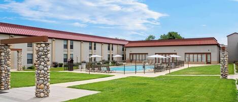 A hotel with a swimming pool, outdoor seating, and stone pillars.
