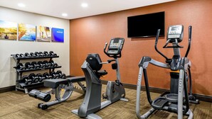 Une salle de sport d’hôtel équipée de tapis de course, d’un appareil elliptique et d’un porte-haltères.
