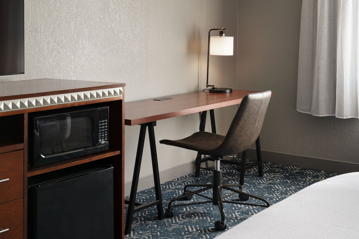 Ein Hotelzimmer mit Bett, Schreibtisch mit Lampe, Mikrowelle und Stuhl.