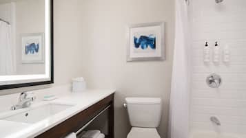 A bathroom with a white sink, a toilet, a shower, and two framed artworks on the wall.