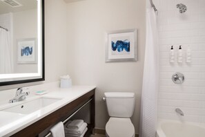 A bathroom with a white sink, a toilet, a shower, and two framed artworks on the wall. - Four Points by Sheraton Tucson Airport (Tucson)