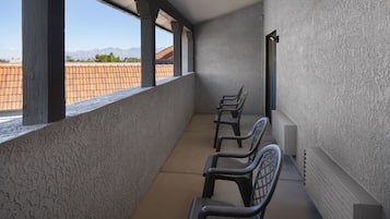 A balcony with a view of a tiled roof and mountains in the distance.
