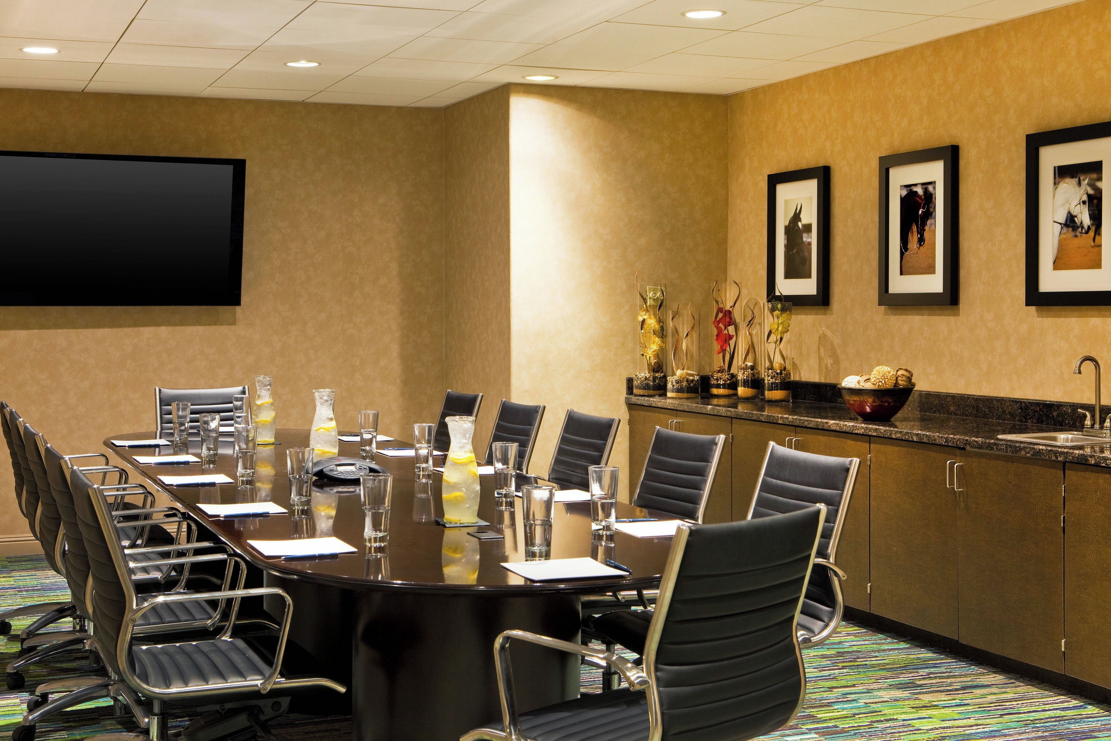 A conference room with a long table, chairs, a projector screen, framed pictures, and a buffet area with a bowl of bread.