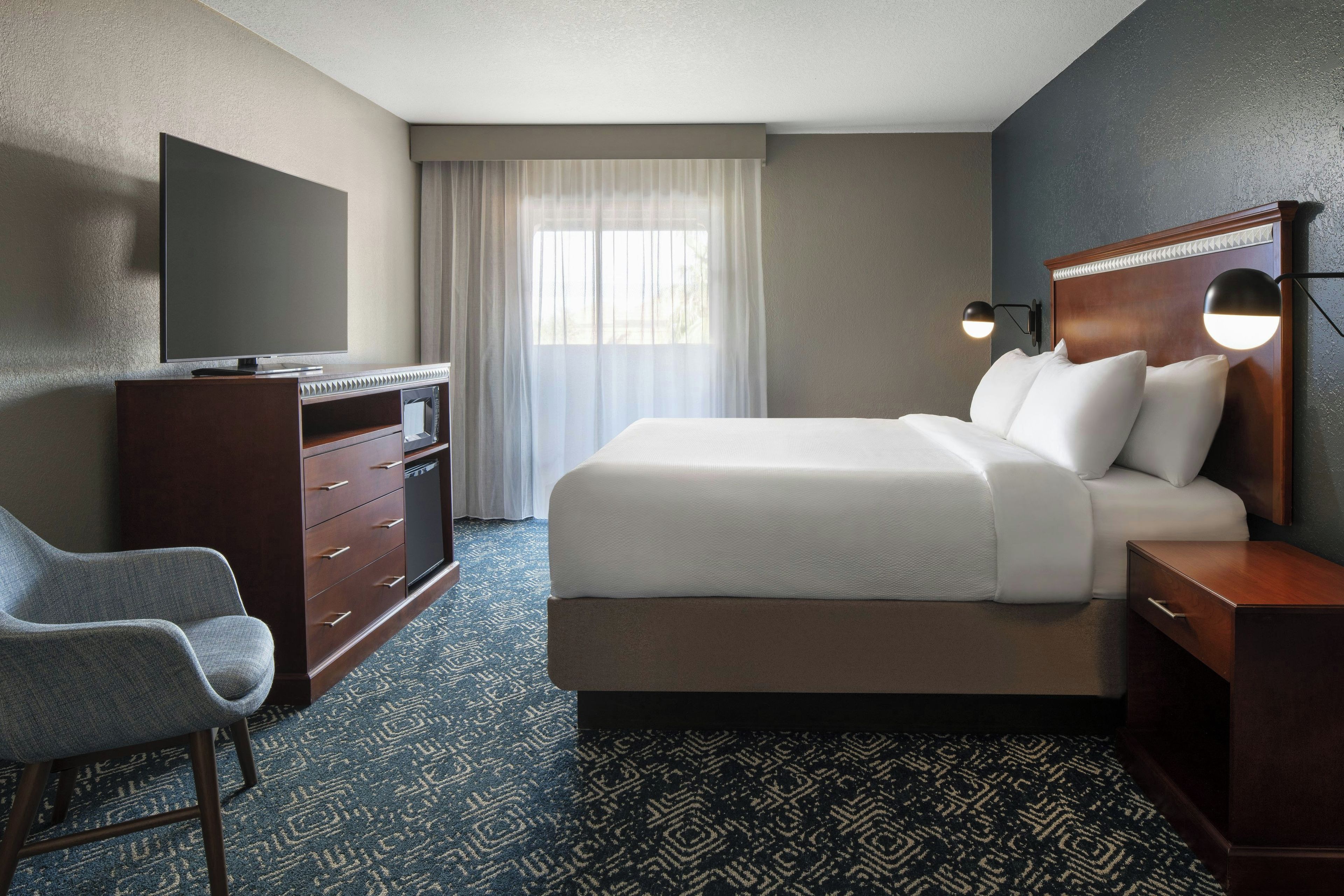 A hotel room with a bed, a desk, a chair, a television, and a window with curtains.