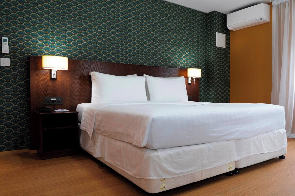 Ein Hotelzimmer mit Bett, Nachttischlampen, einem Nachttisch und einem Wandpapier mit Muster.