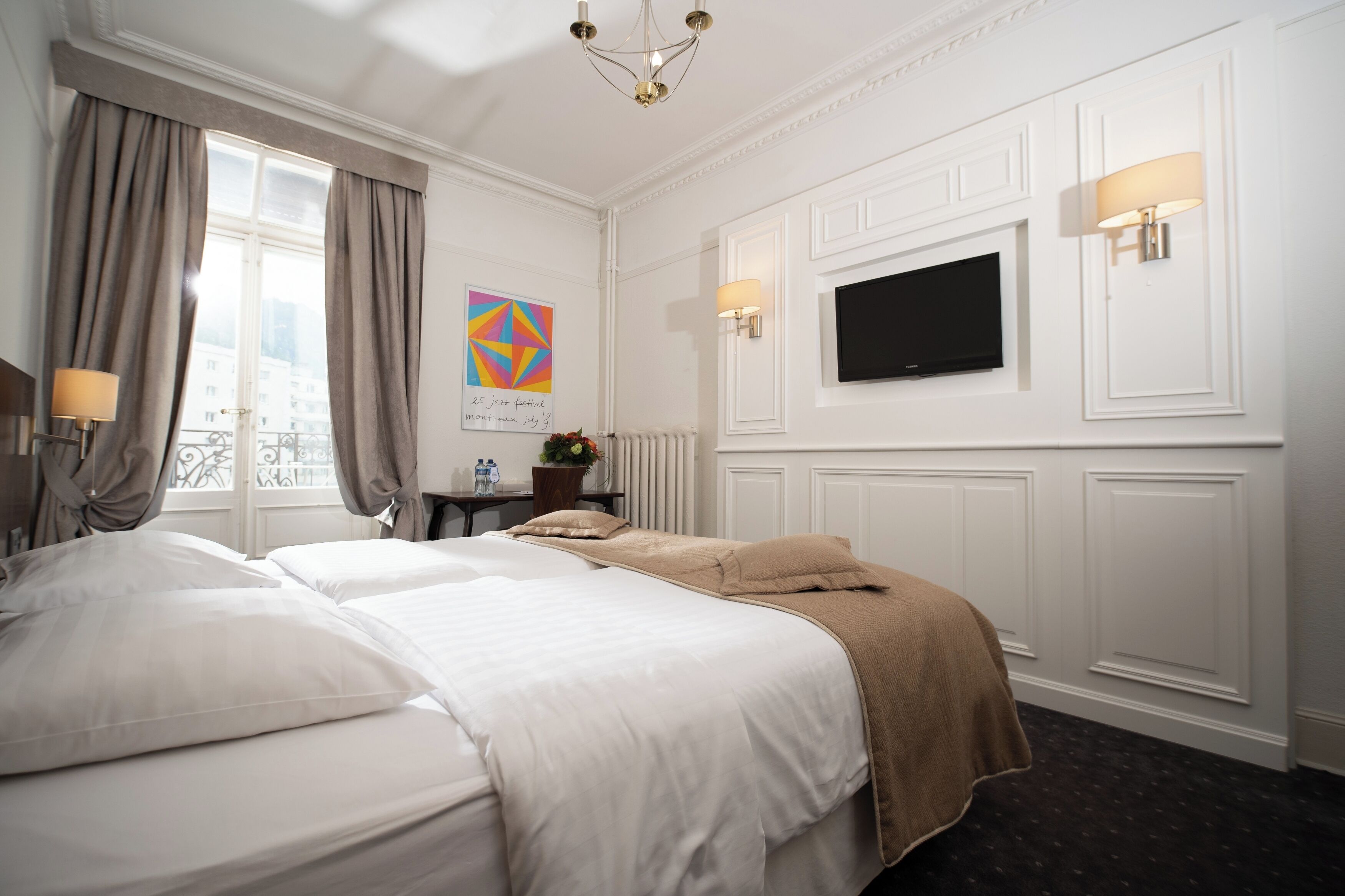 Habitación de hotel con dos camas, televisión, ventana con cortinas, un cuadro y una lámpara.