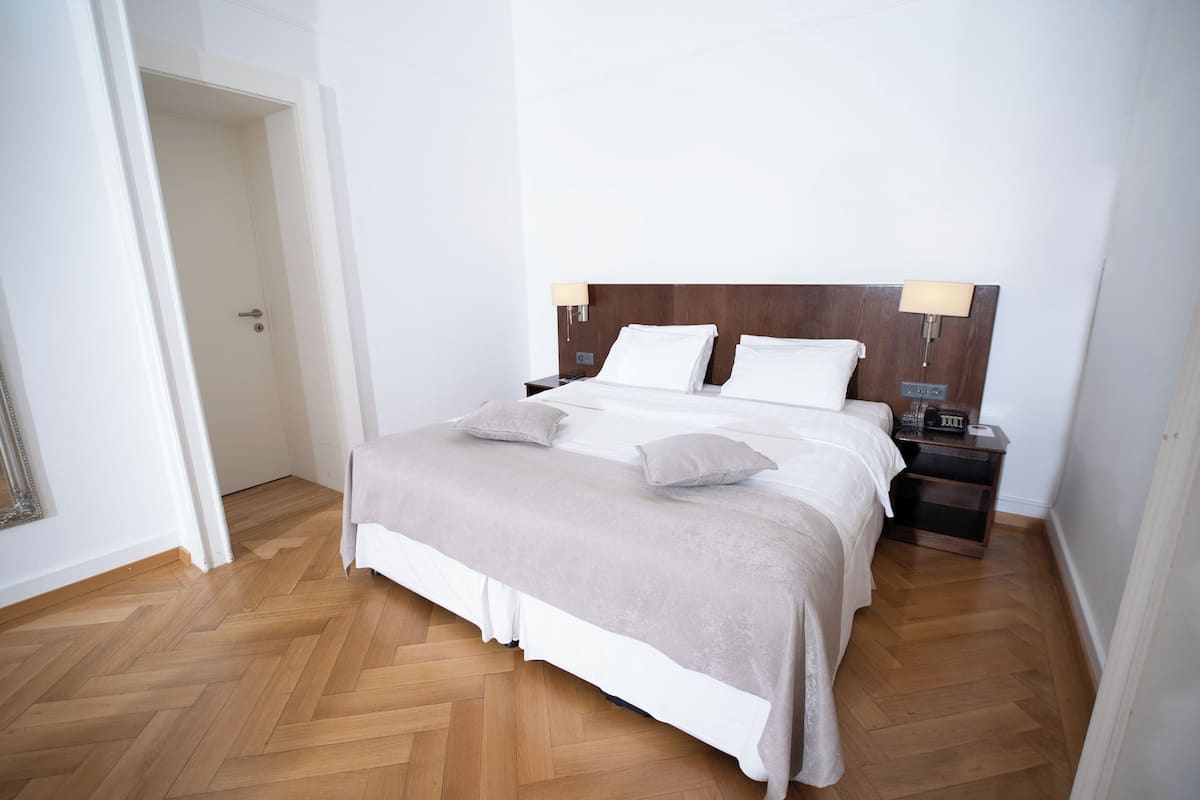 Ein ordentlich bezogenes Bett mit Holz-Kopfteil, zwei Nachttischlampen und einem Nachttisch mit Radio.