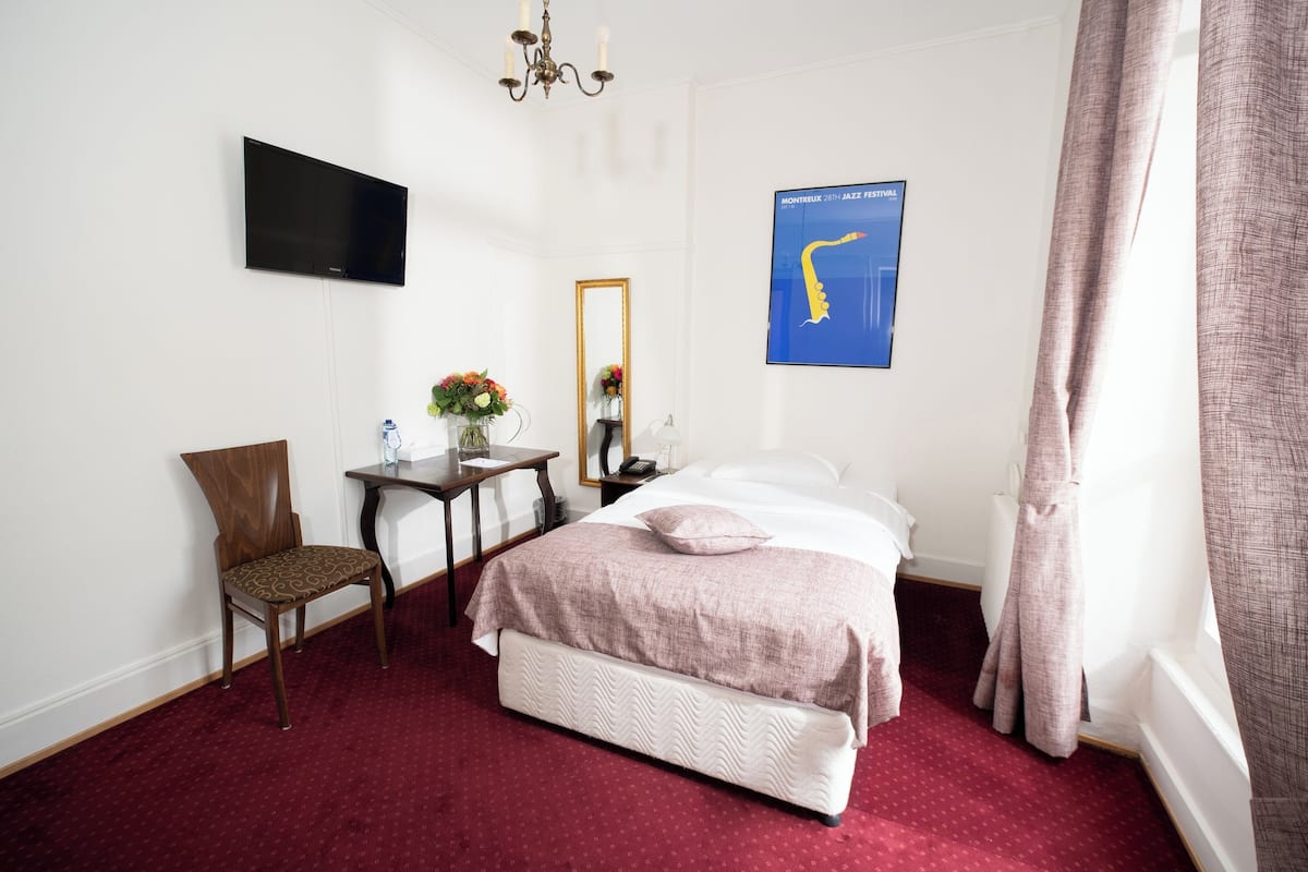 Ein Hotelzimmer mit einem Bett, einem Schreibtisch, einem Sessel, einem Fernseher, einem Spiegel und einem Bild an der Wand.