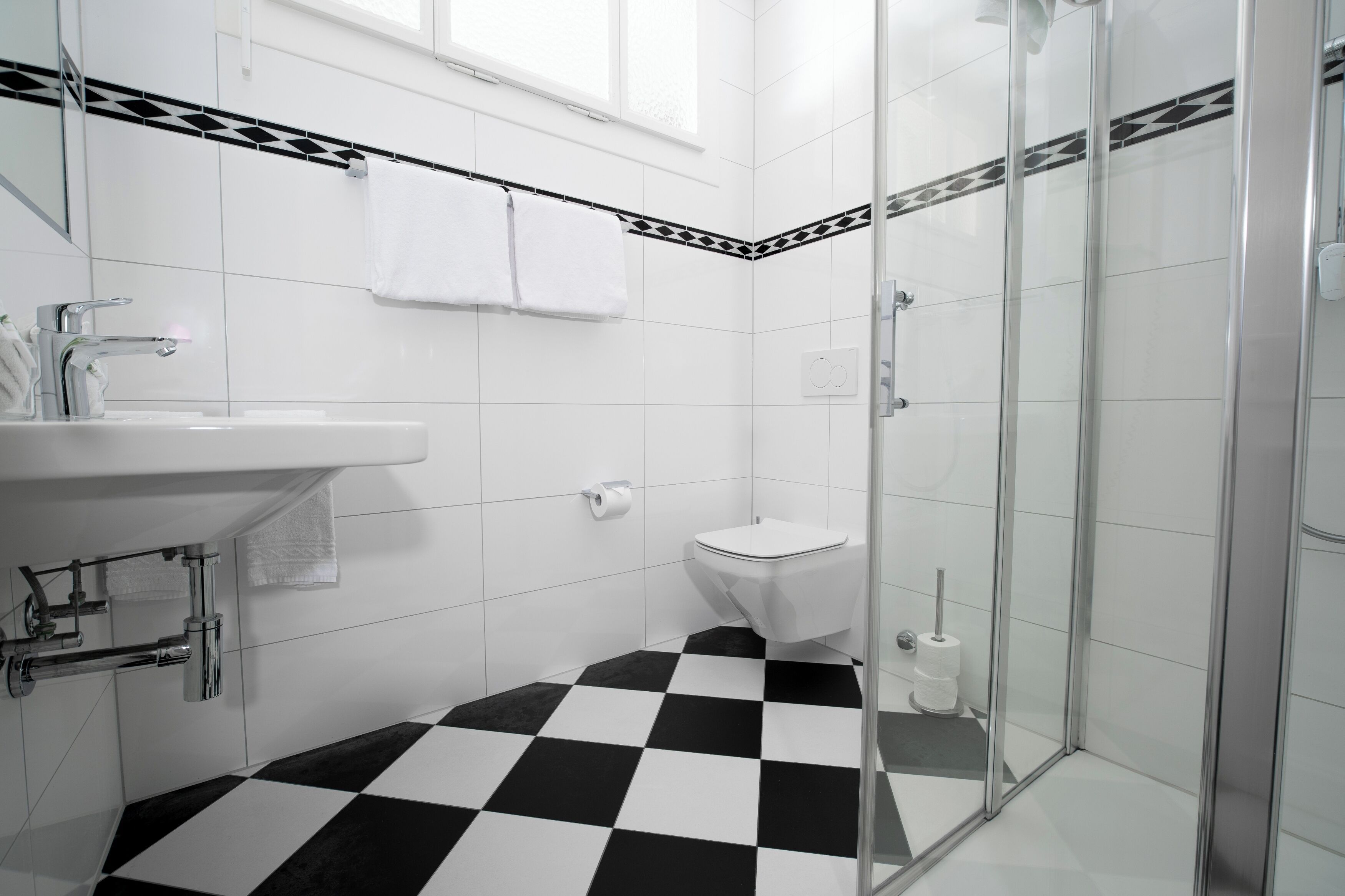 A modern bathroom with a checkered floor, a glass shower enclosure, a white sink, and a toilet.