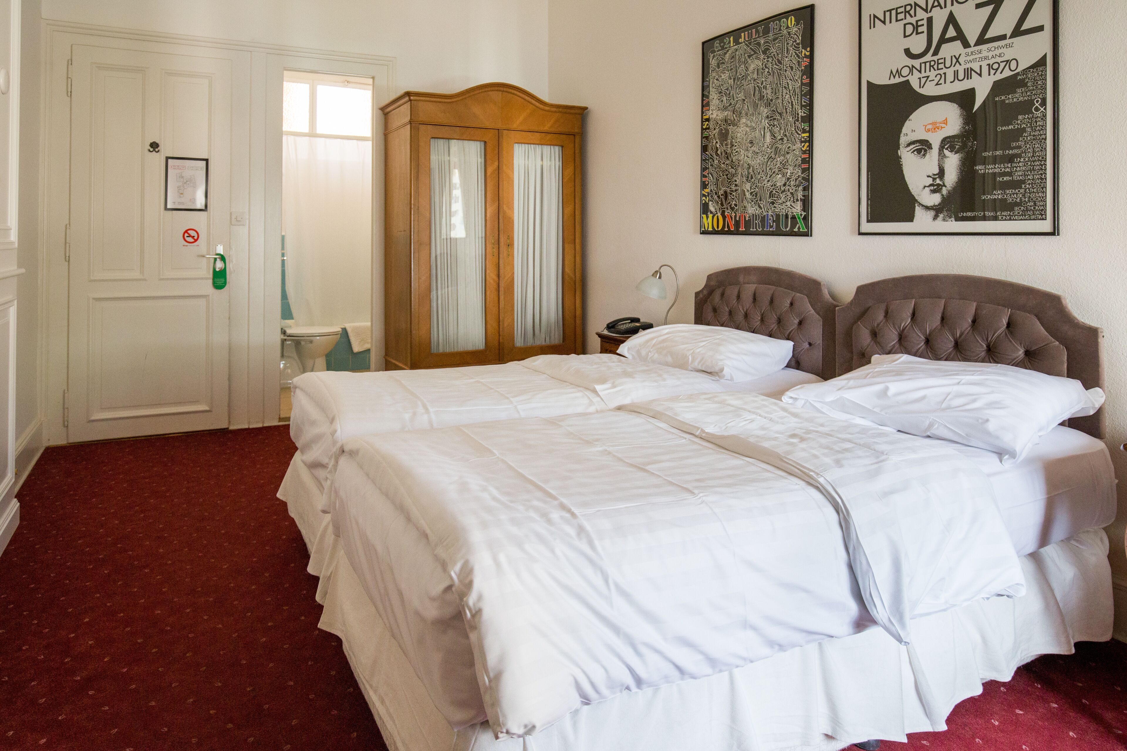 A hotel room with a large bed, a wardrobe, a nightstand, and a poster on the wall.