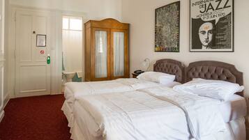 A hotel room with a large bed, a wardrobe, a nightstand, and a poster on the wall.