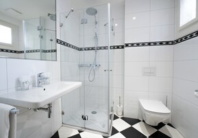Un baño moderno con ducha de vidrio, un lavamanos blanco y un inodoro.