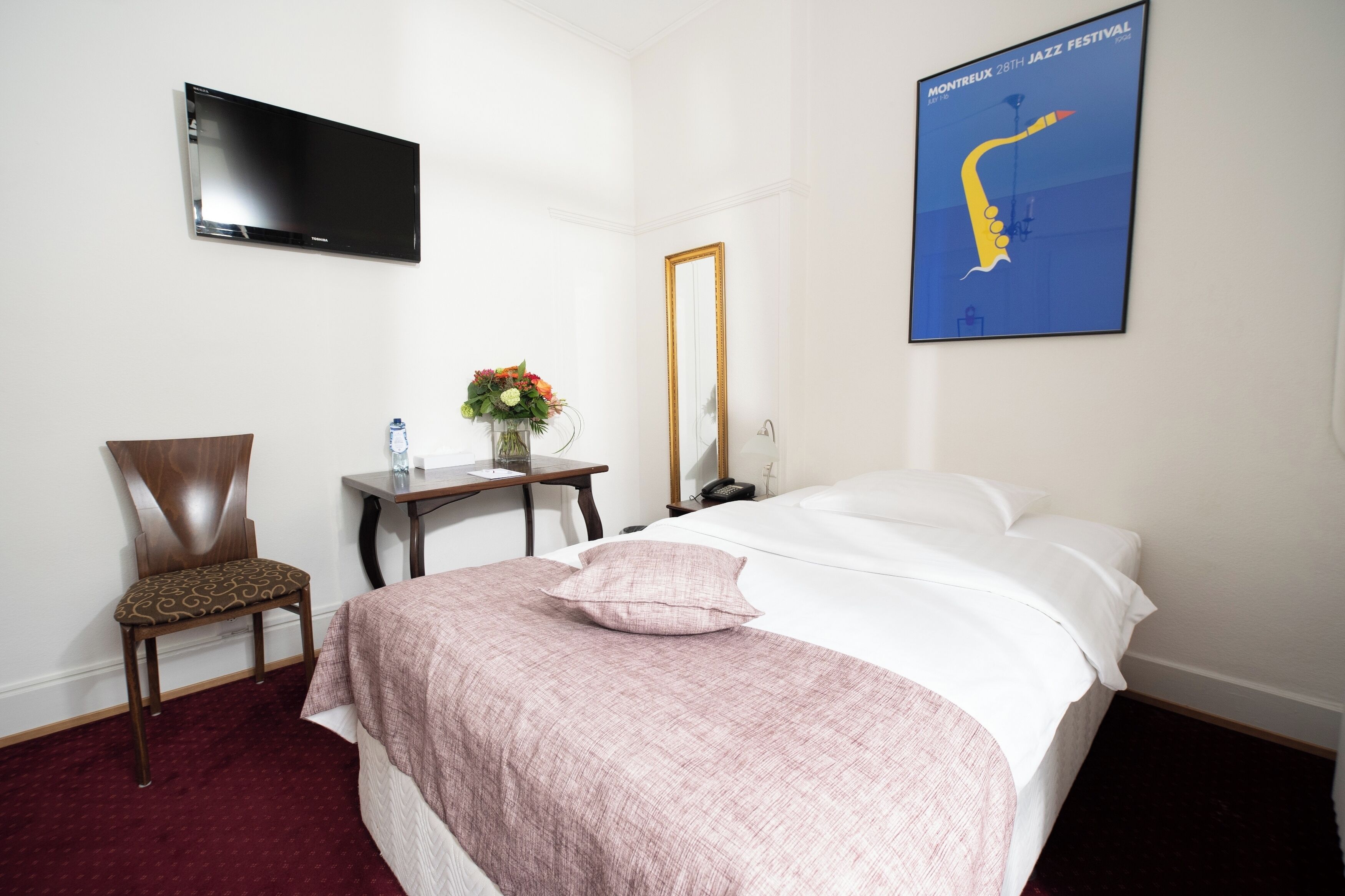 Habitación de hotel con cama, una silla, un escritorio, un espejo, un televisor de pantalla plana y un cartel en la pared.