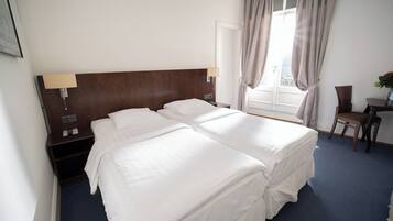 Une chambre d’hôtel avec deux lits, un bureau, une chaise, une fenêtre avec des rideaux et une lampe fixée au mur.