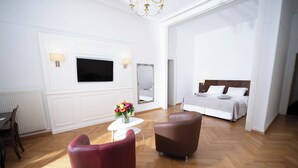 A modern hotel room with a large bed, a TV mounted on the wall, a small table with a vase of flowers, and two leather chairs. - J5 Hotels Helvetie Montreux (Montreux)