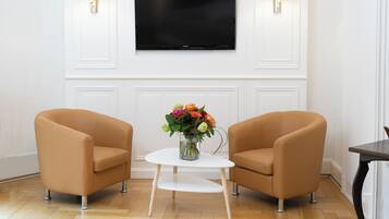 Une pièce comprenant deux fauteuils, une petite table blanche ornée d’un vase de fleurs et un téléviseur à écran plat fixé au mur.