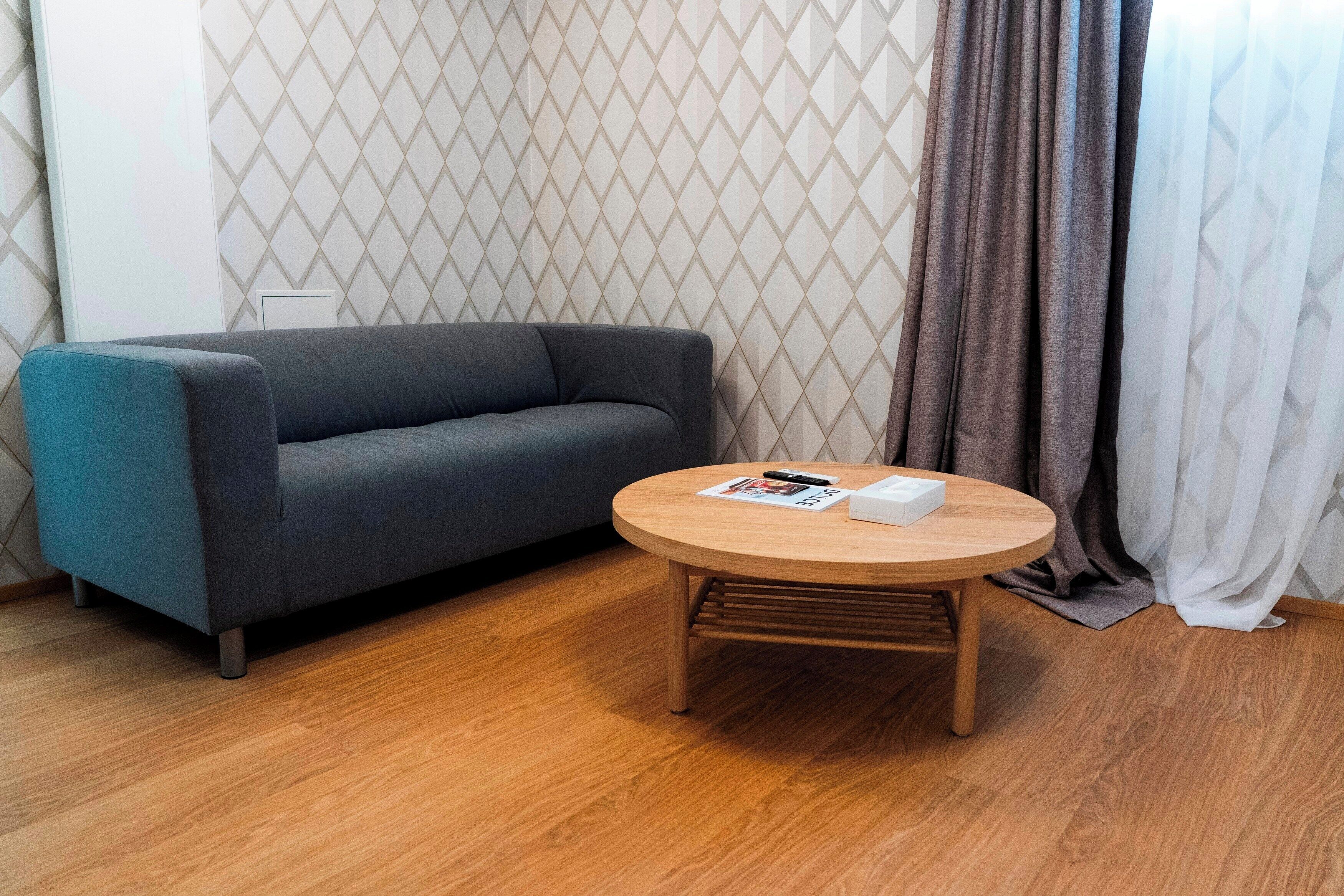 A modern living room with a grey sofa, a wooden coffee table, and a patterned wallpaper.
