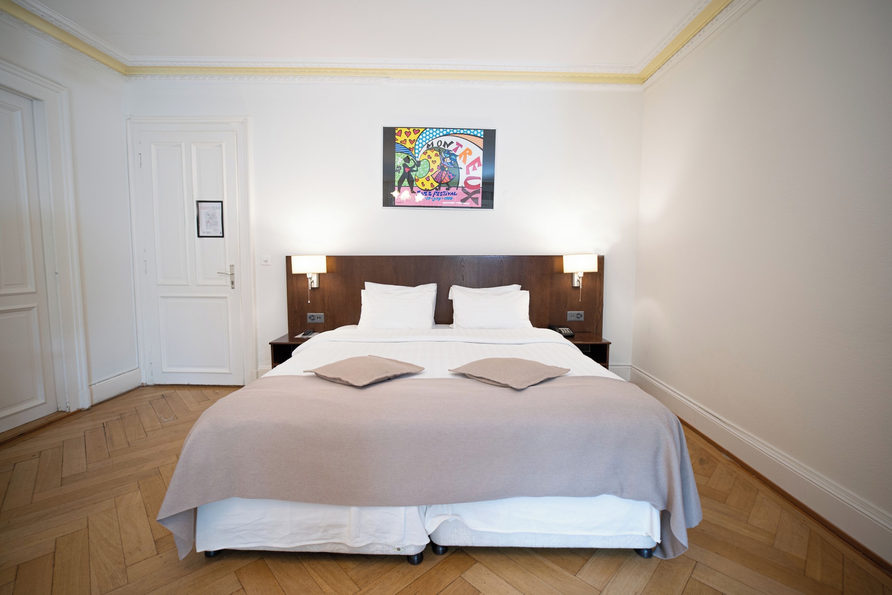 A neatly arranged hotel room with a large bed, two bedside tables, a framed artwork above the bed, and a wooden floor.