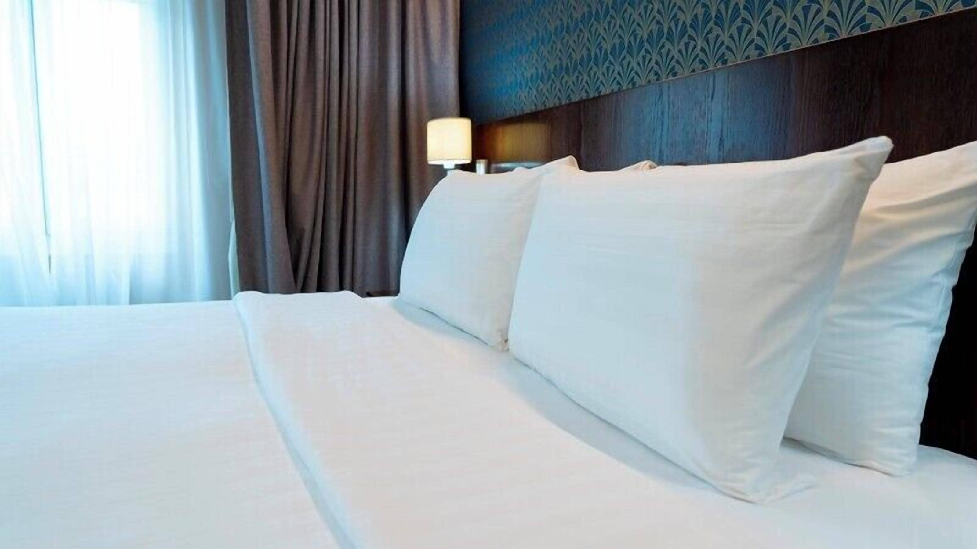 Ein Hotelzimmer mit einem großen Bett, weißen Laken und einem Kopfteil mit einem gemusterten Design.