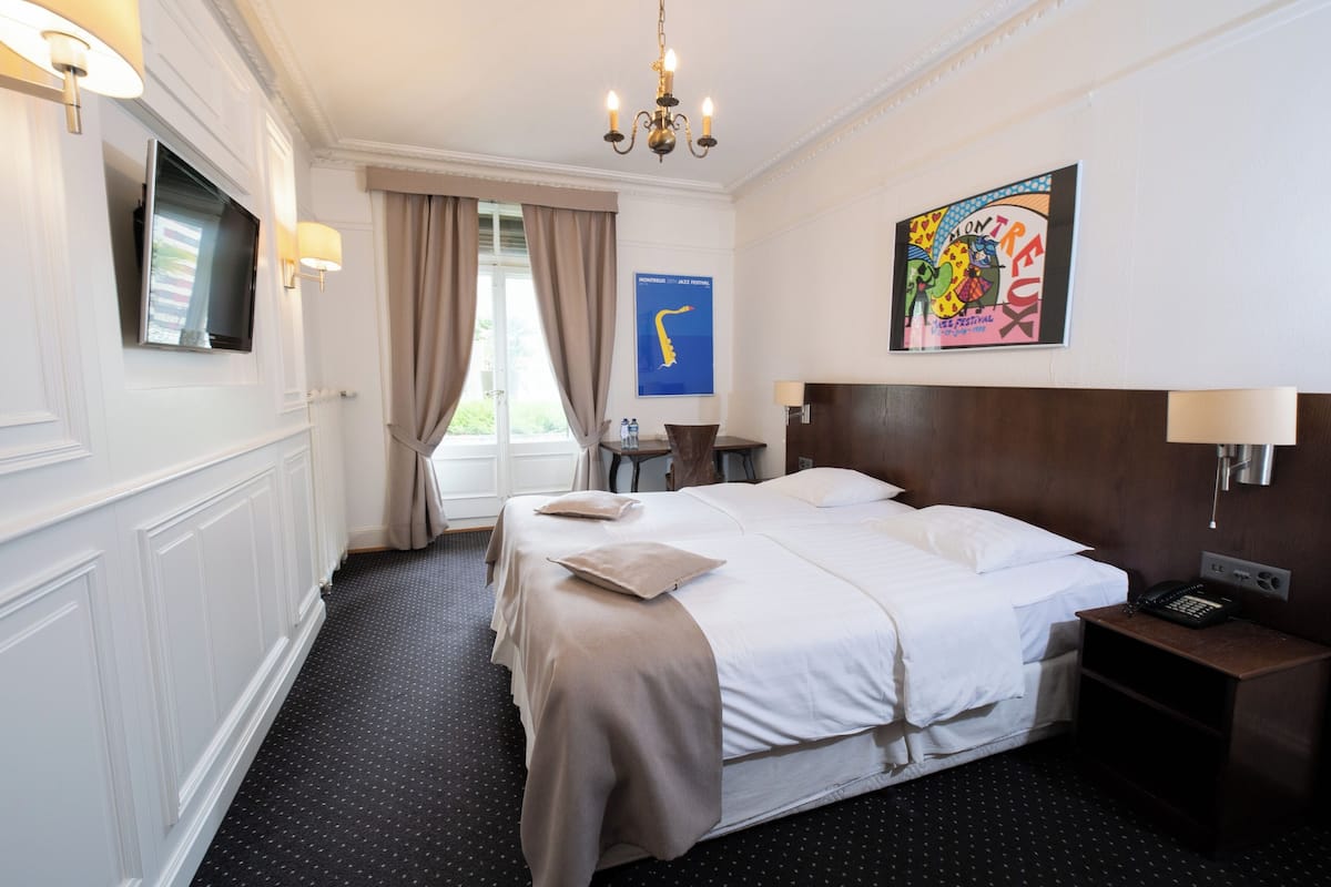 Ein Hotelzimmer mit einem großen Bett, einem Flachbildfernseher, einem Schreibtisch mit Lampe und einem Bild an der Wand.