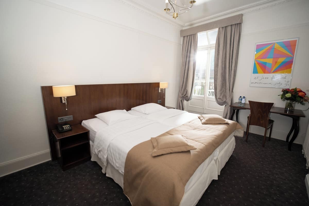 Ein Hotelzimmer mit einem großen Bett, Nachttischlampen, einem Schreibtisch mit Stuhl und einem fenster mit Vorhängen.