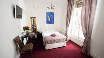 Une chambre d’hôtel équipée d’un lit, d’un bureau, d’une chaise, d’un miroir, d’une télévision et d’une fenêtre avec des rideaux.