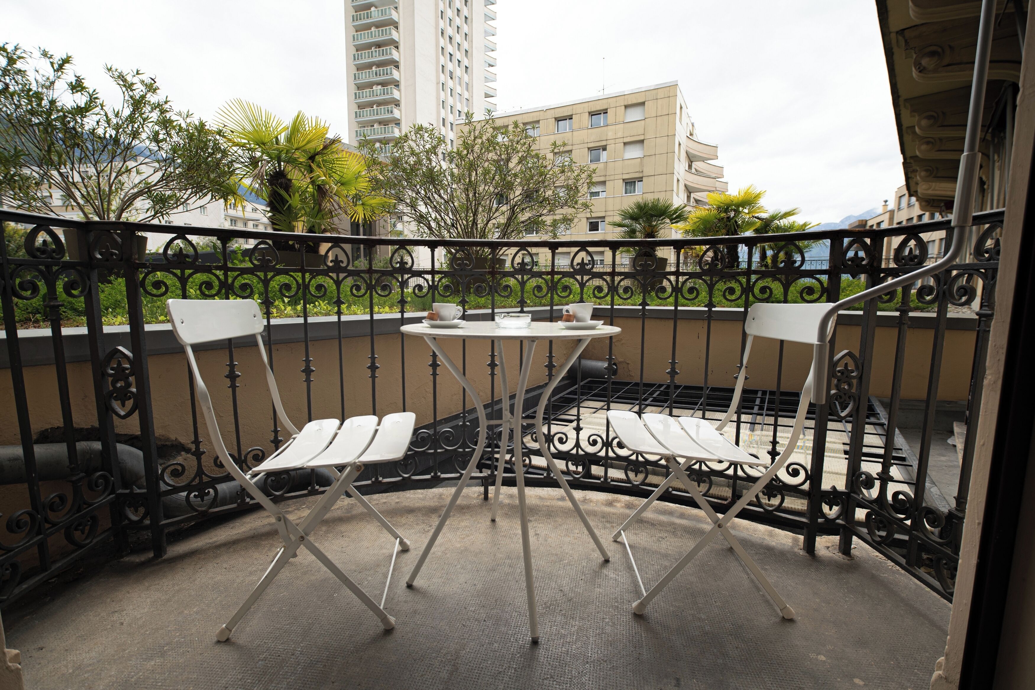 Un balcon avec une petite table et deux chaises, entouré d’une balustrade en fer forgé.