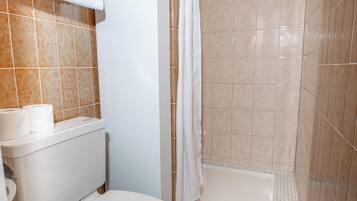A bathroom with a toilet, a shower, and a tiled floor.