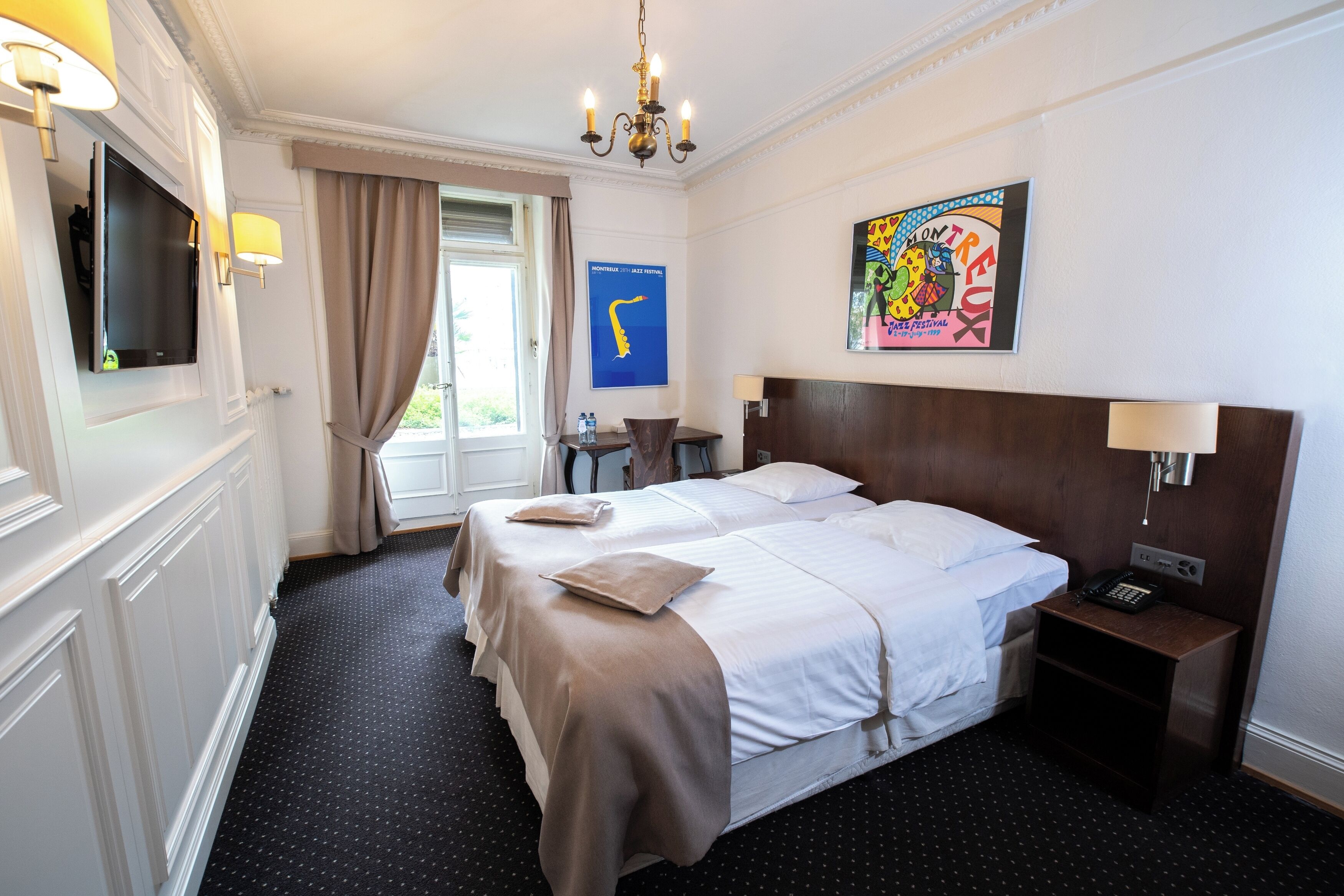 A hotel room with a large bed, bedside tables, a TV, and a painting on the wall.