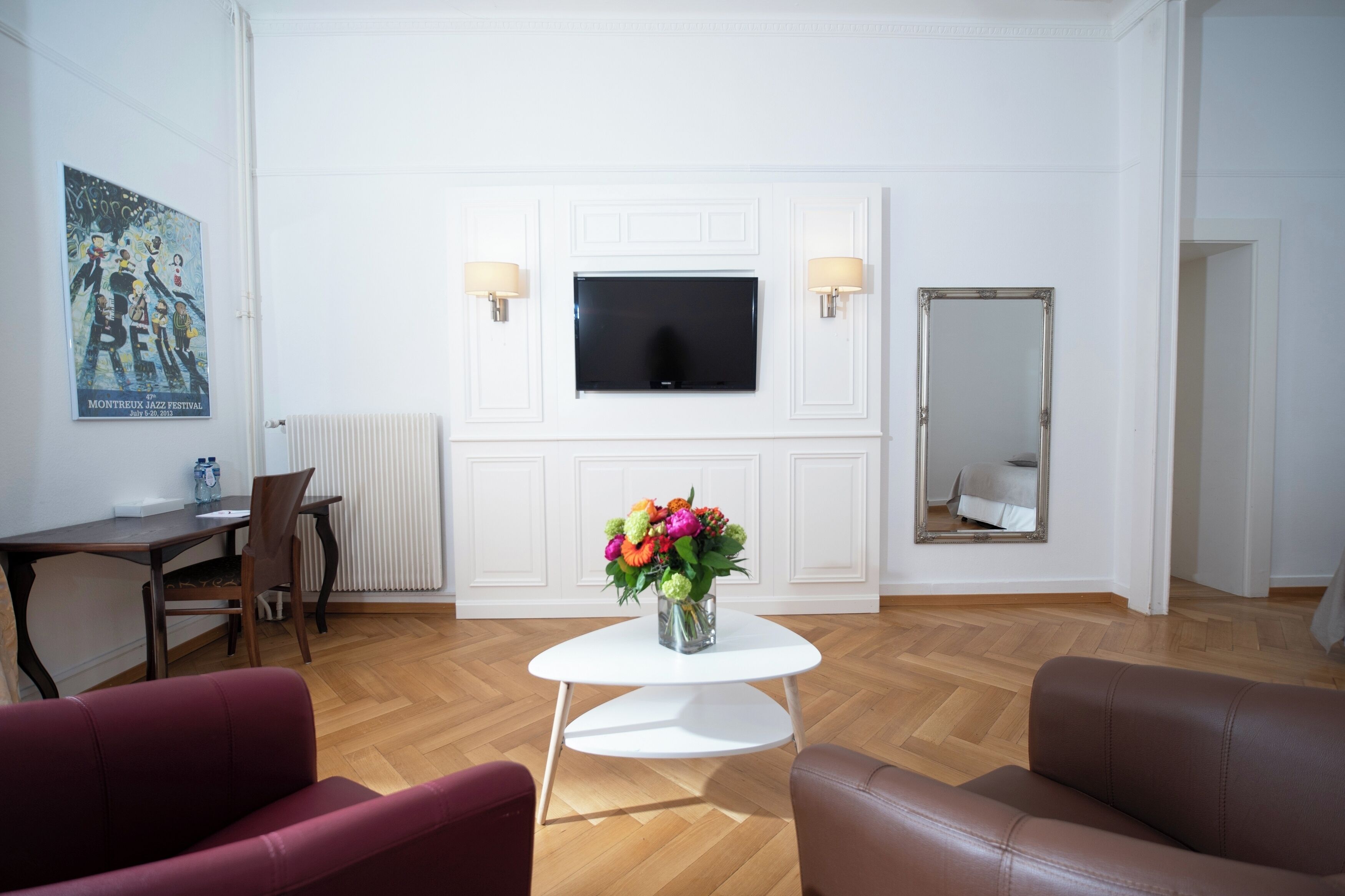 A living room with a white TV, a small table with a vase of flowers, two sofas, and a dining area with a chair and table.