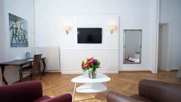 A living room with a white TV, a small table with a vase of flowers, two sofas, and a dining area with a chair and table.