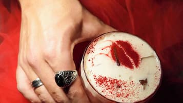 Una mano che tiene un bicchiere con panna montata e un motivo a forma di cuore rosso, su sfondo rosso.