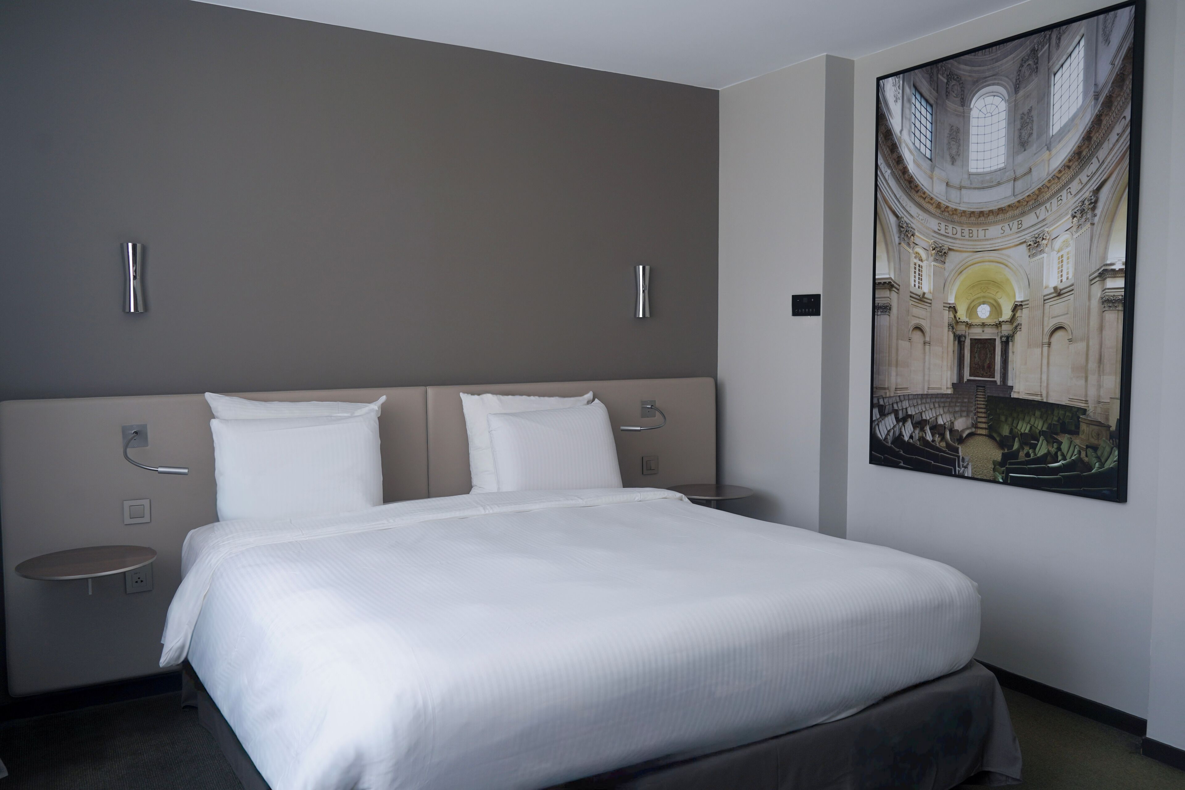A hotel room with a large bed, two bedside tables, and a wall-mounted artwork of a historical building.