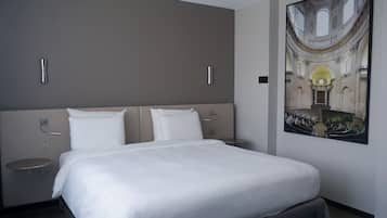 A hotel room with a large bed, two bedside tables, and a wall-mounted artwork of a historical building.