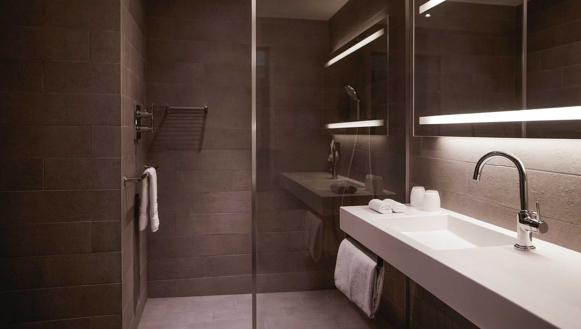 A modern bathroom with a glass shower enclosure, a white sink with a chrome faucet, and a large mirror above the sink.
