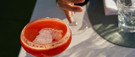 A hand holding a cocktail glass with a frothy drink, and another cocktail glass with a frothy drink in the background.