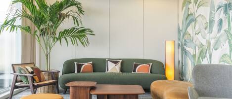 A modern living room with a green sofa, wooden coffee table, and a large potted plant.