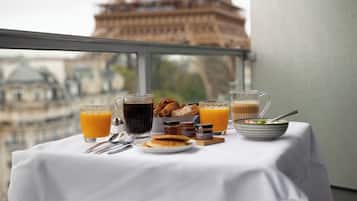 Una mesa de desayuno con diversas bebidas y pasteles, con la Torre Eiffel visible a través de una ventana.