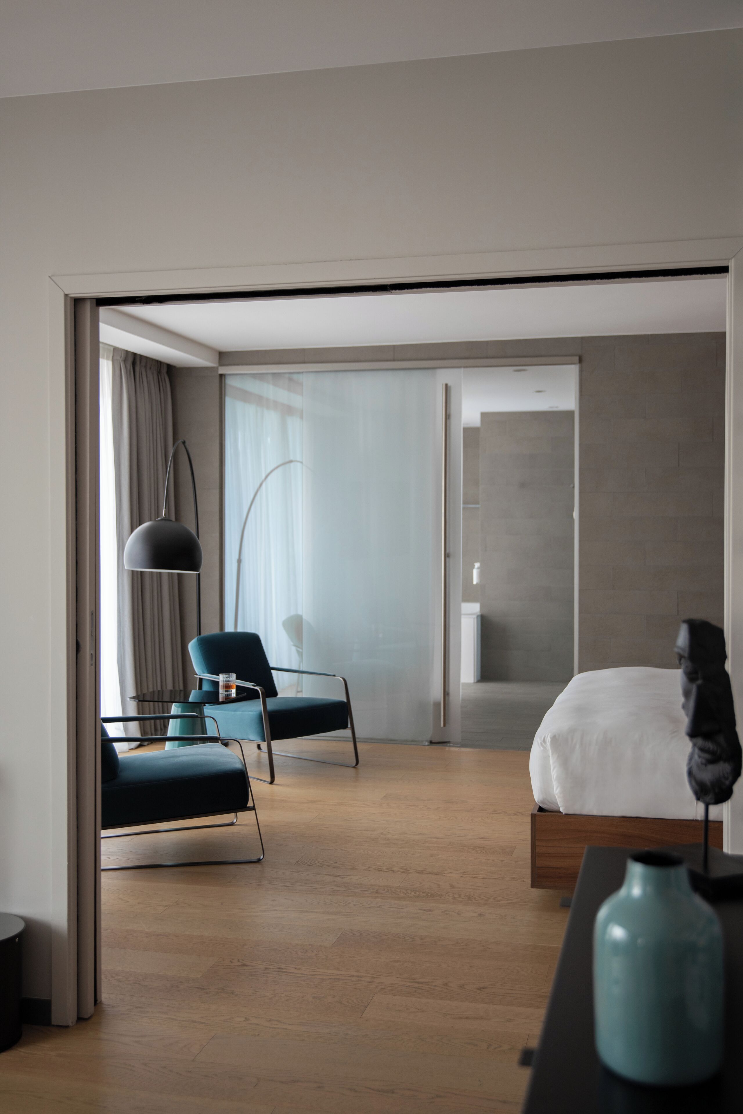 A modern hotel room with a bed, a desk, a chair, and a large window.
