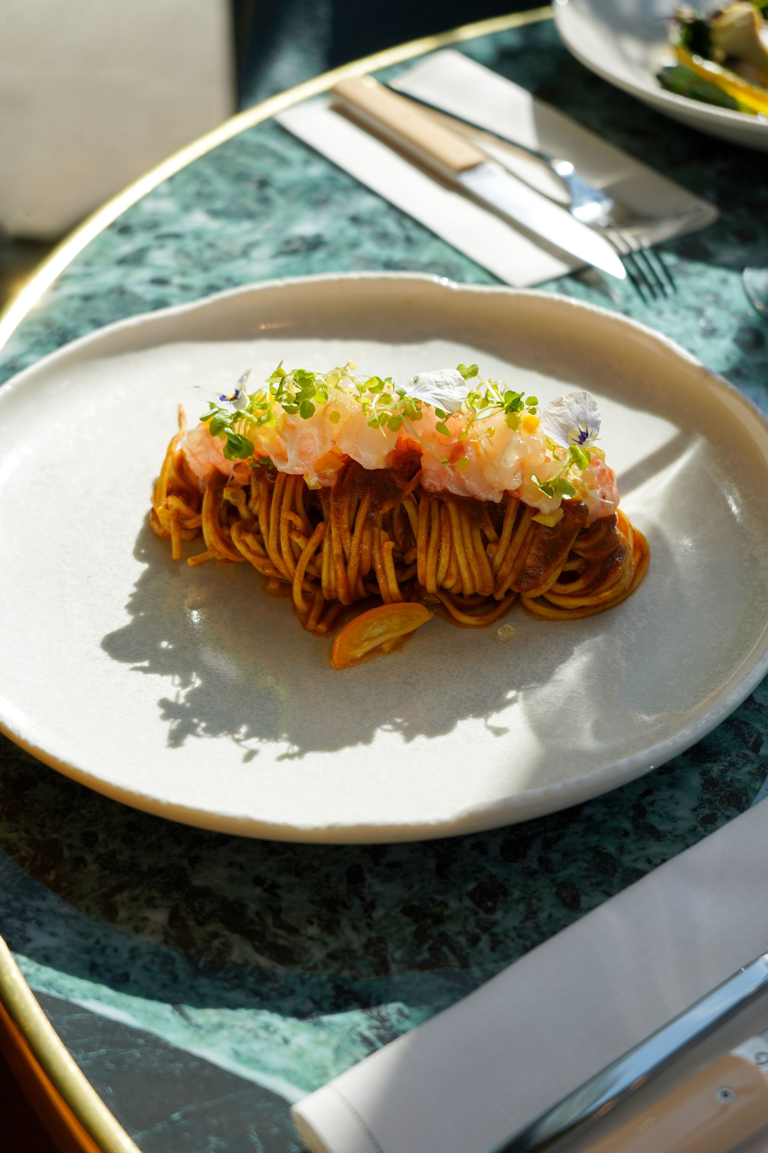 A plate of spaghetti with a topping of shrimp and greens on a marble table.