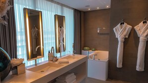 A modern bathroom with a double sink, large mirrors, a bathtub, and two towels hanging on hooks.