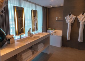 A modern bathroom with a double sink, large mirrors, a bathtub, and two towels hanging on hooks.