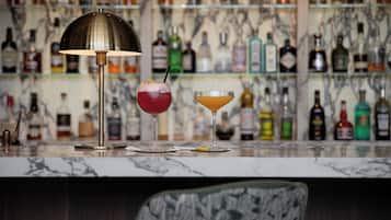 A bar area with a marble countertop, two drinks, a lamp, and a shelf of liquor bottles.